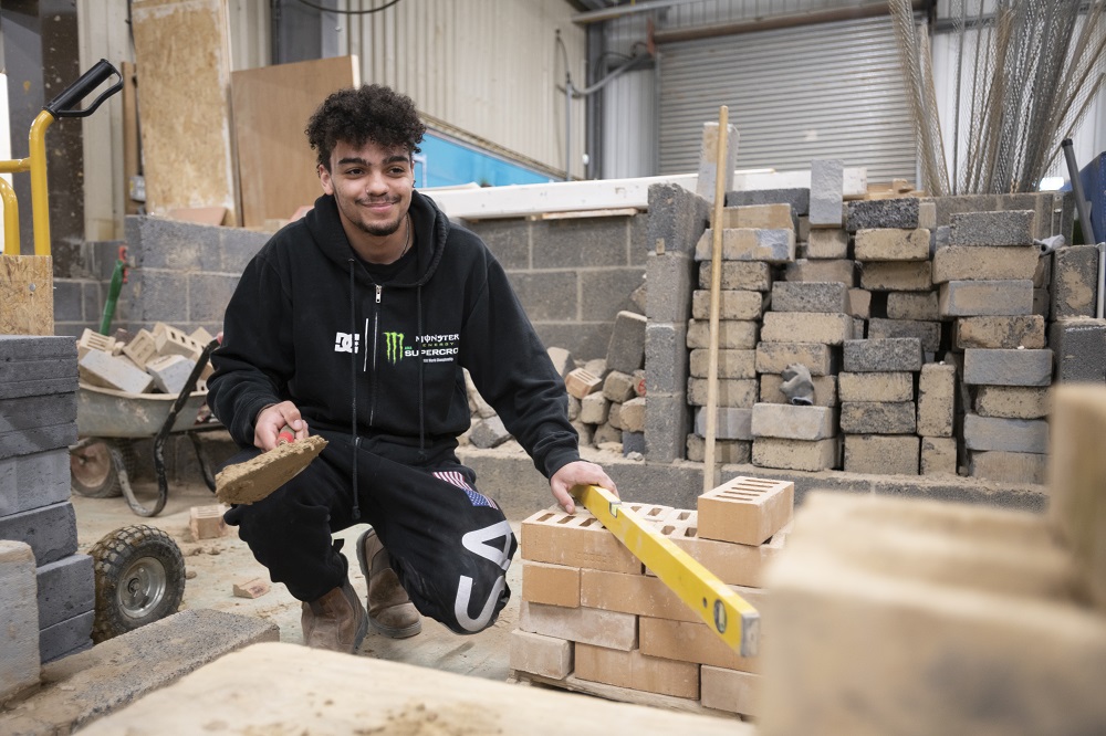 A bricklaying student surrounded by blocks and bricks