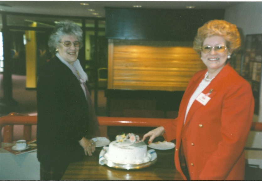 Ann Johnson cutting a cake with a red coat.