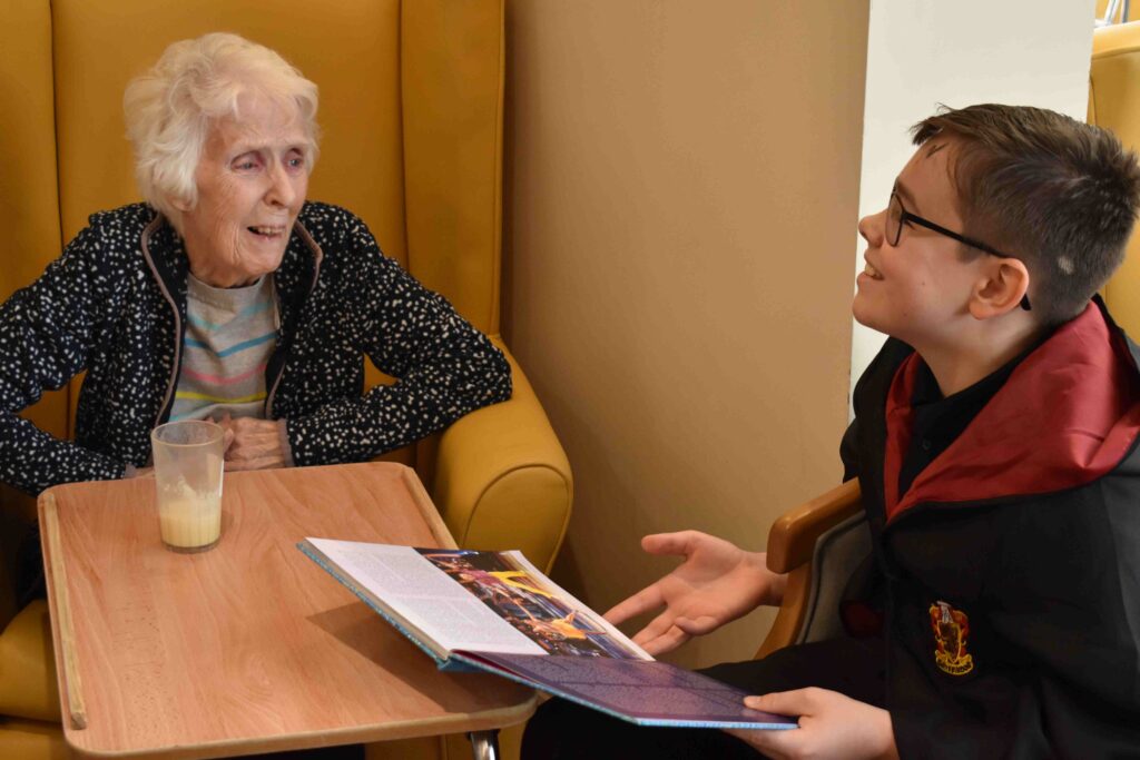 Sullivan from Duke of Lancaster reading a story to a resident at Woodspring House care home in Fakenham