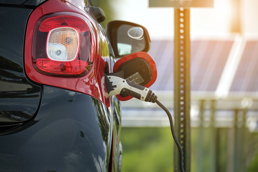 Electric plug-in car charging with electricity from solar renewable power source parked on city street.