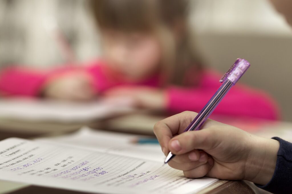 Portrait of cute pretty little serious child girl drawing with pencil on paper on blurred background. Art education, creativity, doing homework and children activities concept.